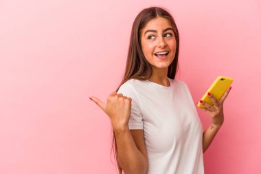 Elinde cep telefonu olan beyaz bir kadın pembe arka plan noktalarına izole edilmiş, baş parmak uzakta, gülen ve kaygısız..