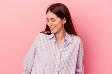 Pembe arka planda izole edilmiş genç beyaz kadın gülüyor ve gözlerini kapıyor, rahatlamış ve mutlu hissediyor..
