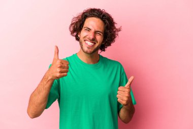 Kafkasyalı genç bir adam pembe fırında izole edilmiş, iki parmağını da kaldırıyor, gülümsüyor ve kendinden emin..