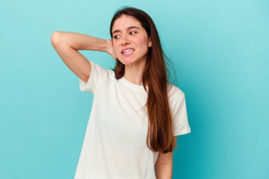 Mavi arka planda izole edilmiş genç beyaz kadın yorgun ve uykulu ellerini başının üstünde tutuyor..