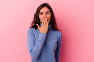 Pembe arka planda izole edilmiş genç beyaz kadın şok olmuş, ağzı ellerle kaplanmış, yeni bir şey keşfetmeye hevesli..