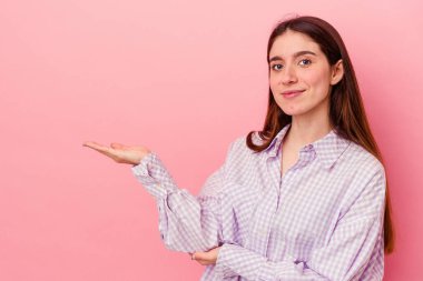 Pembe arka planda izole edilmiş genç beyaz kadın bir avuç içinde fotokopi alanı ve belinde bir el daha gösteriyor..