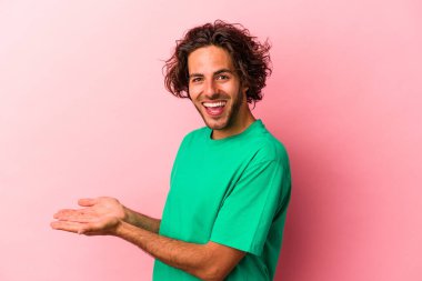 Pembe fırında izole edilmiş genç beyaz bir adam bir palmiye ağacının üzerinde bir kopya alanı tutuyor..