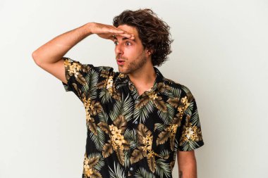 Beyaz arka planda izole edilmiş genç beyaz bir adam uzaklara bakıyor ve elini alnına koyuyor..