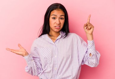 Genç Venezuelalı bir kadın pembe arka planda izole edilmiş ve elinde bir ürün taşıyor..