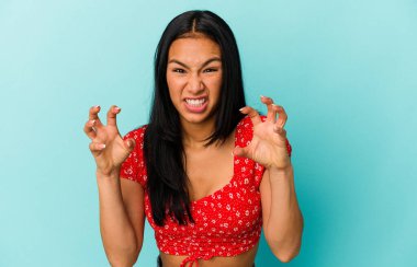 Genç Venezuelalı bir kadın mavi arka planda izole edilmiş gergin elleriyle çığlık atıyor..