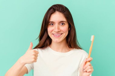 Mavi arka planda diş fırçası tutan beyaz bir kadın.