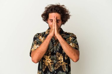 Beyaz arka planda izole edilmiş genç beyaz bir adam el ele tutuşup, ağız kenarında dua ediyor, kendinden emin..