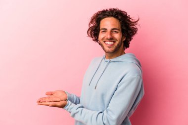 Pembe fırında izole edilmiş genç beyaz bir adam bir palmiye ağacının üzerinde bir kopya alanı tutuyor..