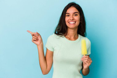 Mavi arka planda dondurması olan beyaz bir kadın. Elinde mavi arka planda izole edilmiş bir dondurma tutan beyaz bir kadın. Gülümsüyor ve boş alanda bir şeyler gösteriyor..