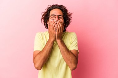 Pembe fırında izole edilmiş genç beyaz bir adam bir şeye gülüyor, elleriyle ağzını kapatıyor..