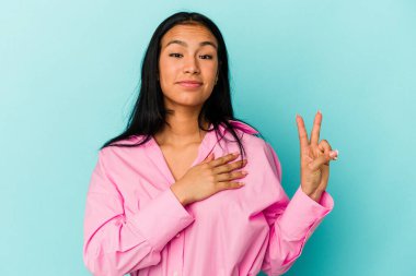 Genç Venezuelalı bir kadın mavi arka planda izole edilmiş yemin ediyor, elini göğsüne koyuyor..