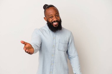Sakallı Afro-Amerikan bir adam pembe arka planda izole edilmiş, elini kameraya uzatarak selamlama hareketi yapıyor..