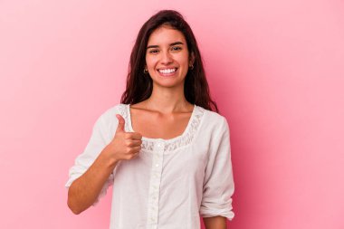 Pembe arka planda izole edilmiş genç beyaz kadın gülümsüyor ve başparmağını kaldırıyor.