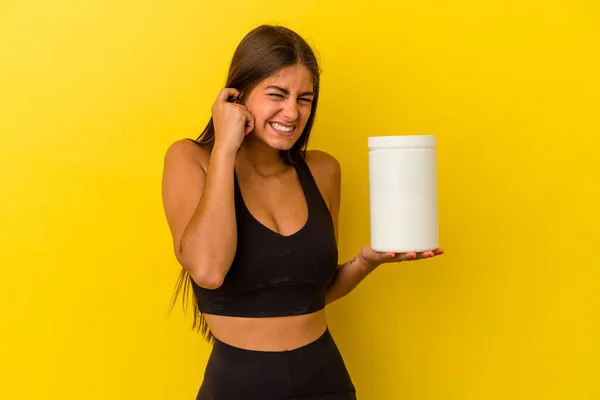 手で耳を覆う黄色の背景に単離されたタンパク質ボトルを保持若い白人女性 — ストック写真