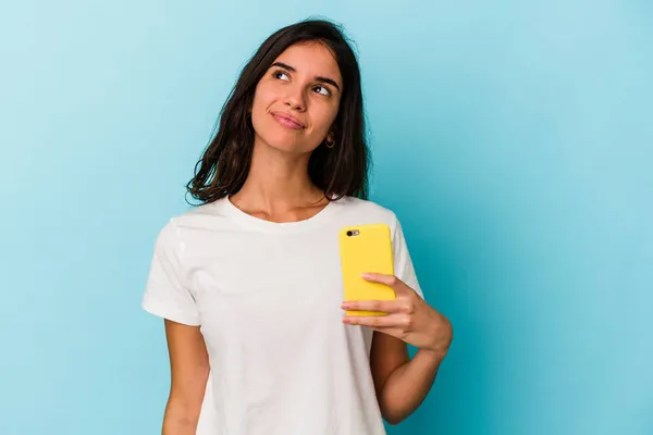 Ung Kaukasiska Kvinna Som Håller Mobiltelefon Isolerad Blå Bakgrund Drömmer — Stockfoto