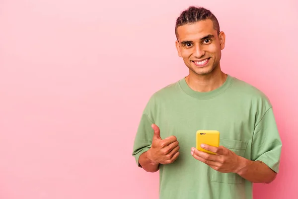 Młody Wenezuelczyk Trzymający Telefon Komórkowy Różowym Tle Uśmiechnięty Podnoszący Kciuk — Zdjęcie stockowe