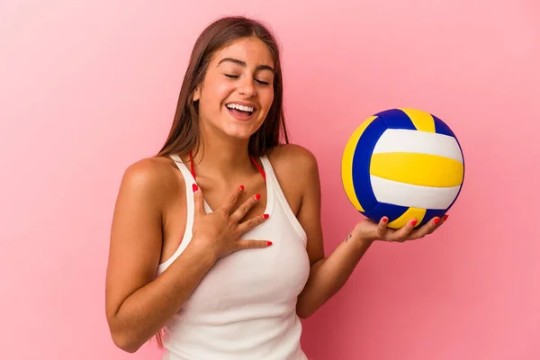 年轻的高加索女人拿着一个粉色背景的排球球 大声笑着把手放在胸前 — 图库照片
