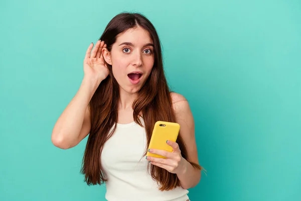 Ung Kaukasisk Kvinna Håller Mobiltelefon Isolerad Blå Bakgrund Försöker Lyssna — Stockfoto