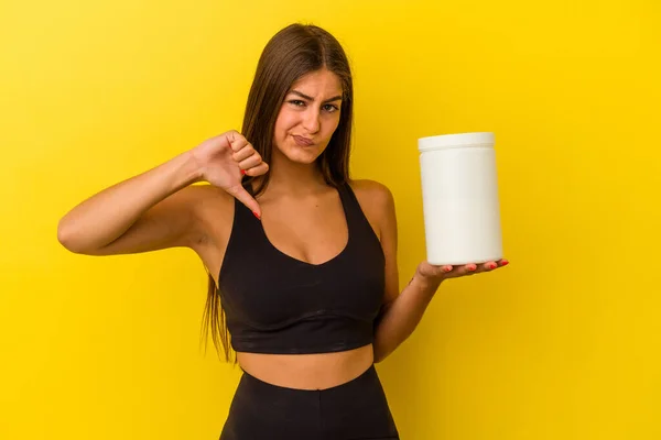 黄色の背景に単離されたタンパク質ボトルを保持若い白人女性は嫌いなジェスチャーを示す 親指ダウン 意見の相違 — ストック写真