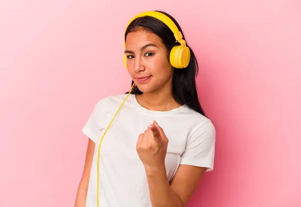 年轻的委内瑞拉女人听着被粉色背景隔离的音乐 用手指指指着你 好像在邀请你走近 — 图库照片