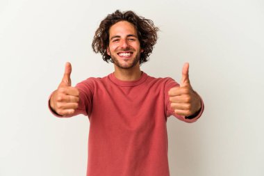 Beyaz arka planda izole edilmiş genç beyaz adam gülümsüyor ve başparmağını kaldırıyor.