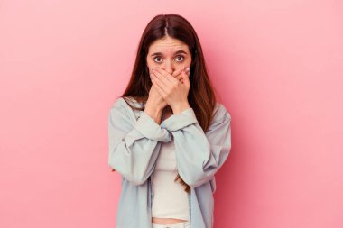 Pembe arka planda izole edilmiş genç, beyaz bir kadın elleri endişeli bir şekilde ağzı örtüyor..