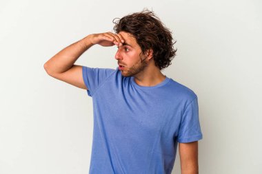 Beyaz arka planda izole edilmiş genç beyaz bir adam uzaklara bakıyor ve elini alnına koyuyor..