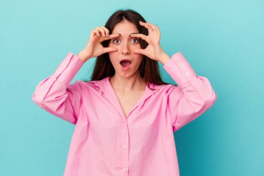 Mavi arka planda izole edilmiş genç beyaz kadın bir başarı fırsatı bulmak için gözlerini açık tutuyor..