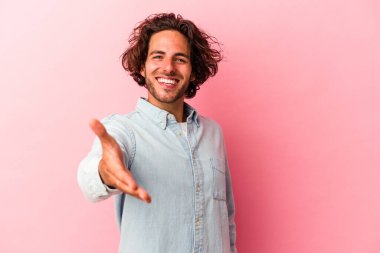 Genç beyaz adam pembe fırında izole edilmiş kameraya elini uzatarak selam veriyor..