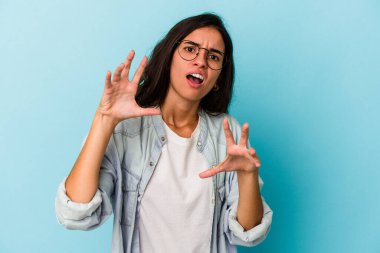 Mavi arka planda izole edilmiş genç beyaz kadın gergin elleriyle çığlık atıyor..