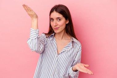 Pembe arka planda izole edilmiş genç beyaz kadın kollarıyla ölçek oluşturuyor, mutlu ve kendinden emin hissediyor..