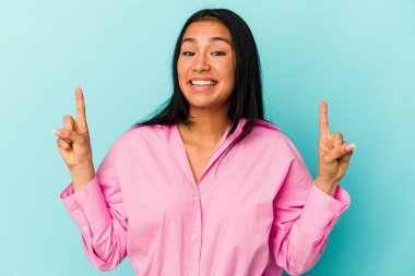 Mavi arka planda izole edilmiş genç Venezuelalı kadın iki parmağı da boş bir alan gösteriyor..