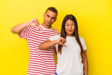 Sarı arka planda izole edilmiş genç latin çift hoşlanmadıkları bir jest gösteriyor, başparmakları aşağıda. Anlaşmazlık konsepti.