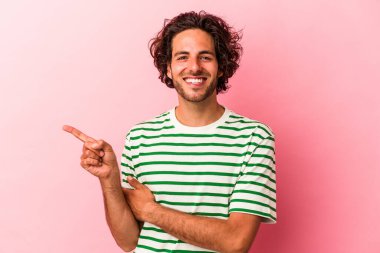Pembe fırında izole edilmiş genç beyaz adam işaret parmağıyla işaret ederek gülümsüyor..