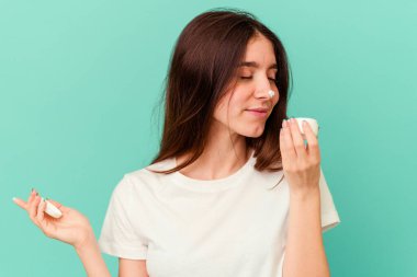 Mavi arka planda, elinde yüz kremi tutan beyaz bir kadın.