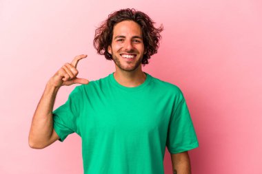 Kafkasyalı genç adam pembe fırında izole edilmiş. Elinde parmakları olan küçük bir şey tutuyor, gülümsüyor ve kendinden emin..