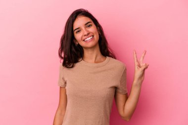 Genç beyaz kadın pembe arka planda izole edilmiş neşeli ve kaygısız parmakları olan bir barış sembolü gösteriyor..