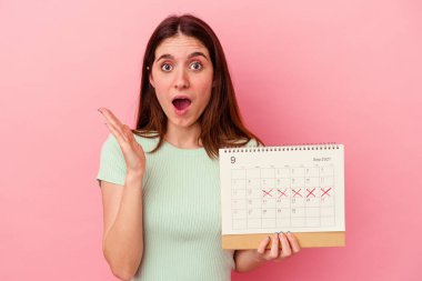 Pembe arka planda bir takvim tutan genç beyaz kadın şaşırdı ve şok oldu..