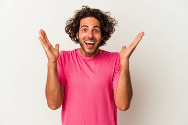 Beyaz arka planda izole olmuş genç beyaz bir adam zaferi veya başarıyı kutluyor, şaşırıyor ve şok oluyor..