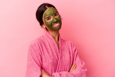 Pembe arka planda yalıtılmış bornoz ve yüz maskesi takan beyaz bir kadın.