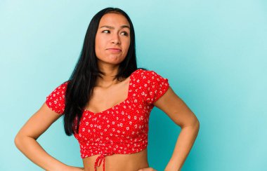 Genç Venezuelalı kadın mavi arka planda izole edilmiş hedeflerine ve amaçlarına ulaşma hayali kuruyor.