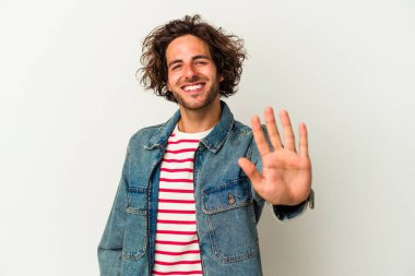 Beyaz arka planda izole edilmiş genç beyaz bir adam gülümseyerek beş numarayı parmaklarıyla gösteriyor..