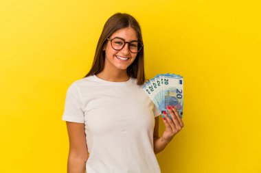 Sarı arka planda izole edilmiş banknotları tutan genç beyaz kadın mutlu, güler yüzlü ve neşeli..