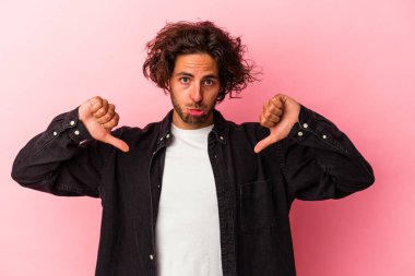 Pembe fırında izole edilmiş genç beyaz bir adam hoş olmayan bir jest yapıyor, başparmakları aşağıda. Anlaşmazlık konsepti.