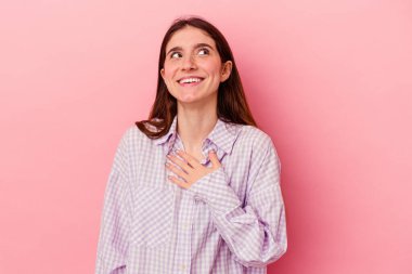 Pembe arka planda soyutlanmış beyaz bir kadın yüksek sesle gülüyor ve elini göğsüne koyuyor..