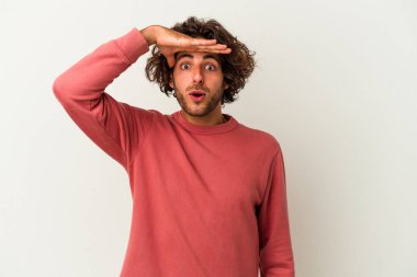 Beyaz arka planda izole edilmiş genç beyaz bir adam uzaklara bakıyor ve elini alnına koyuyor..