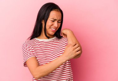 Genç Venezuelalı kadın pembe arka planda izole edilmiş dirsek masajı yapıyor, kötü bir hareketin ardından acı çekiyor..