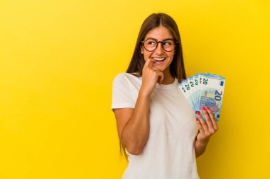 Sarı arka planda izole edilmiş banknotlar tutan genç beyaz kadın bir şeyin fotokopi odasına baktığını düşünerek rahatladı..