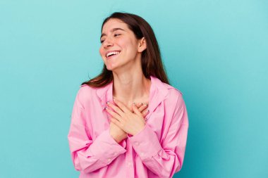 Mavi arka planda soyutlanmış genç beyaz kadın gülüyor, elini yüreğine koyuyor, mutluluk kavramını koruyor..